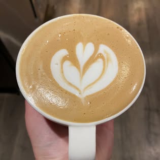 A latte with heart-shaped latte art held by a barista